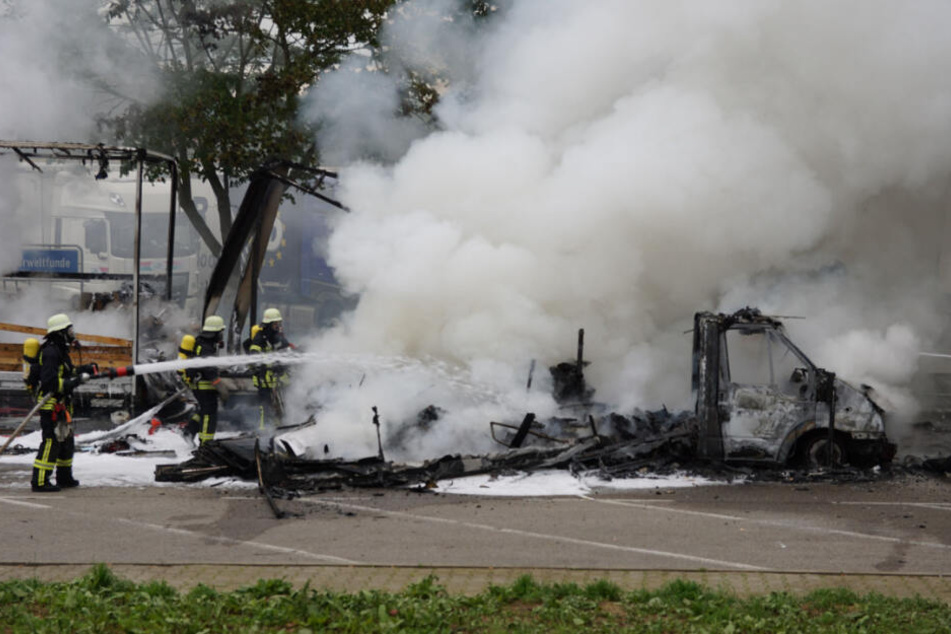 Feuerwehrleute löschen das Wohnmobil mit einem Schlauch.