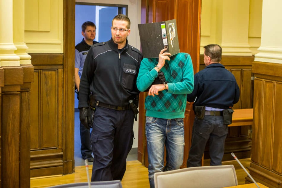 Ein Wachtmeister führt den hinter einem Aktenordner versteckten Dirk K. in den Gerichtssaal.