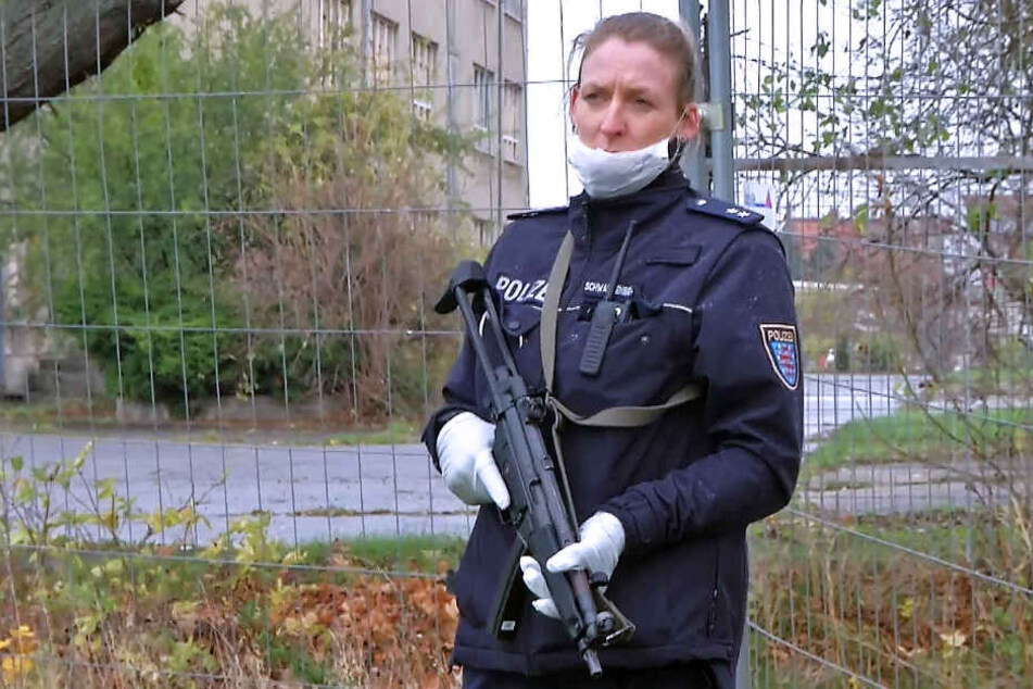 Eine bewaffnete Polizistin sichert die Durchsuchungsmaßnahmen.