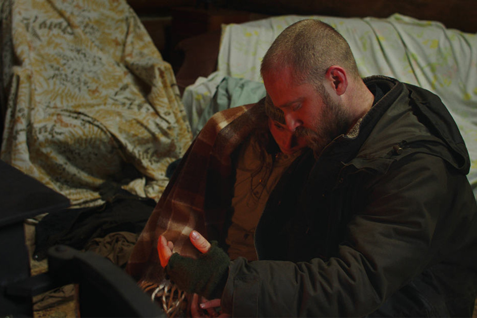 Tom (l., Thomasin McKenzie) und Will (r., Ben Foster) wärmen sich in einem Waldhaus am Kamin auf.