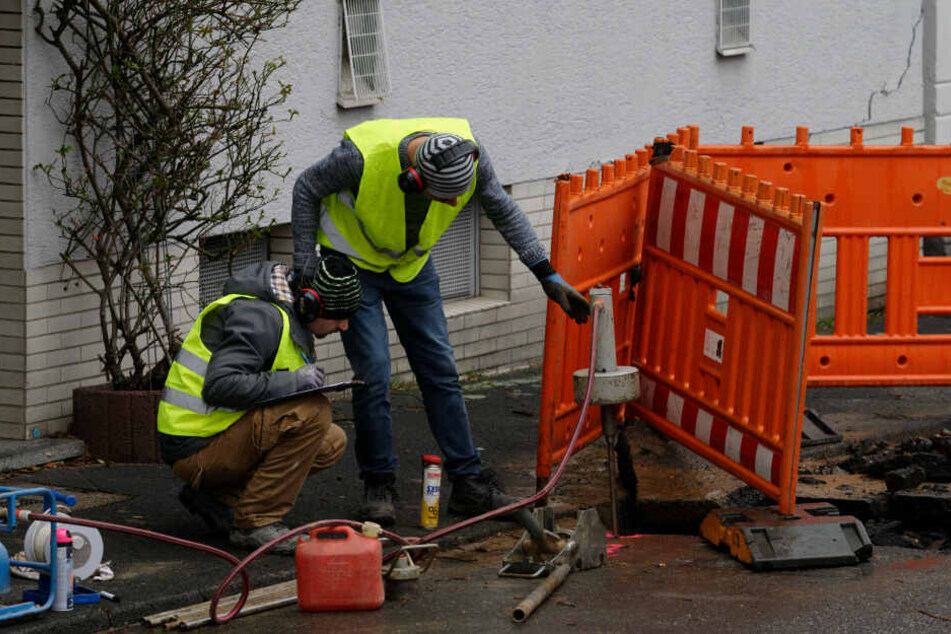 Zwei Männer untersuchen vor einem vom Einsturz bedrohtem Haus den Untergrund.
