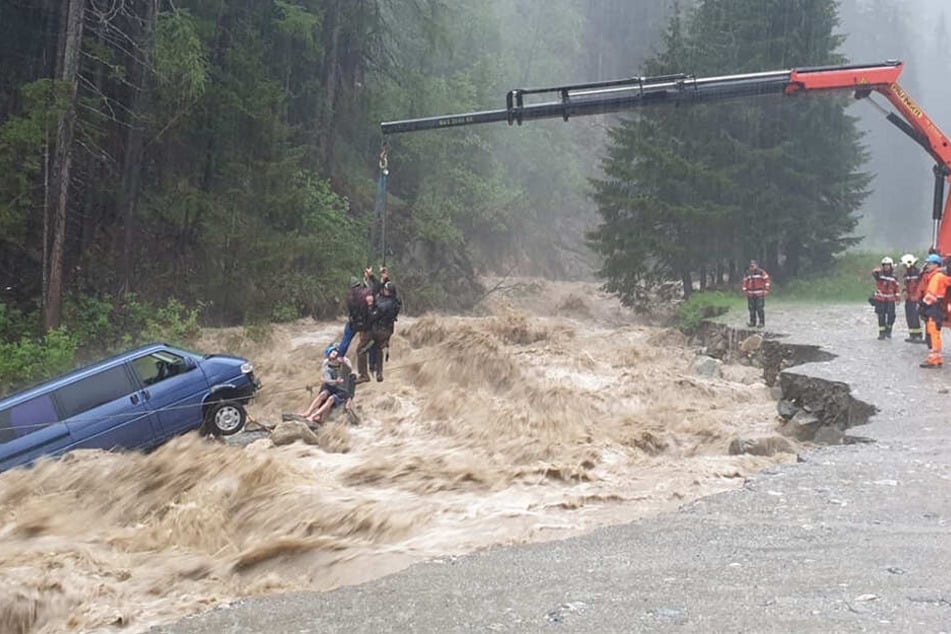 Rettungskräfte heben mit einem Kranfahrzeug zwei deutsche Touristen aus dem Auto, das vom reißenden Hüscherabach mitgerissen wurde.
