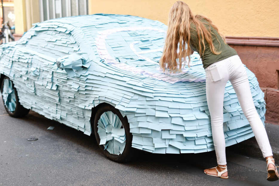 Eine Mitarbeitern der Initiative gegen Falschparken hüllt ein Auto mit Post-it-Zetteln ein. Die Stadt Heidelberg hatte das Fahrzeug extra für die Aktion dort abgestellt. (Archivbild)