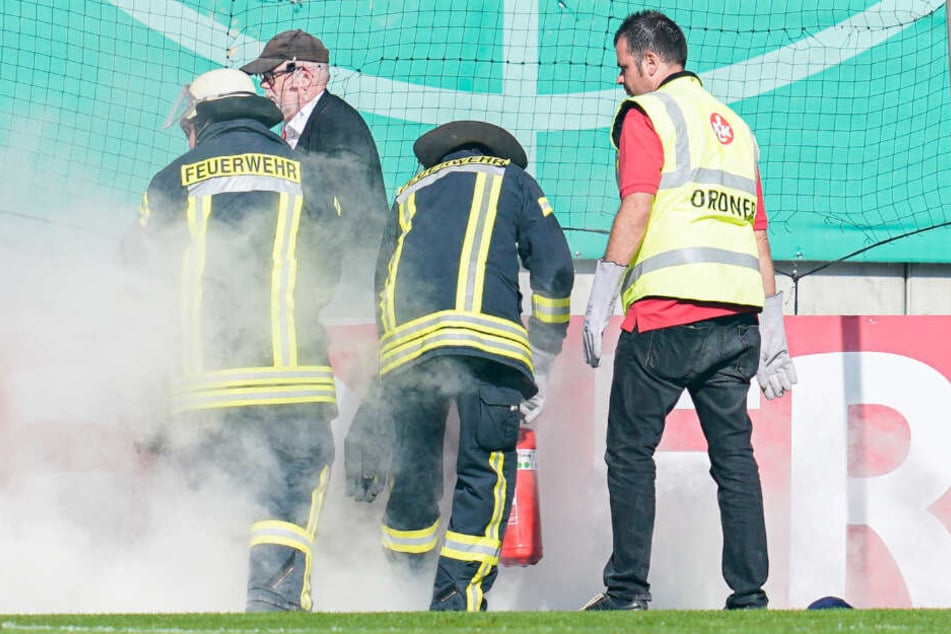 Feuerwehrleute löschen am 10.08.2019 beim Spiel gegen Kaiserslautern brennende Bengalos, die von Mainzer Fans aufs Spielfeld geworfen wurden.