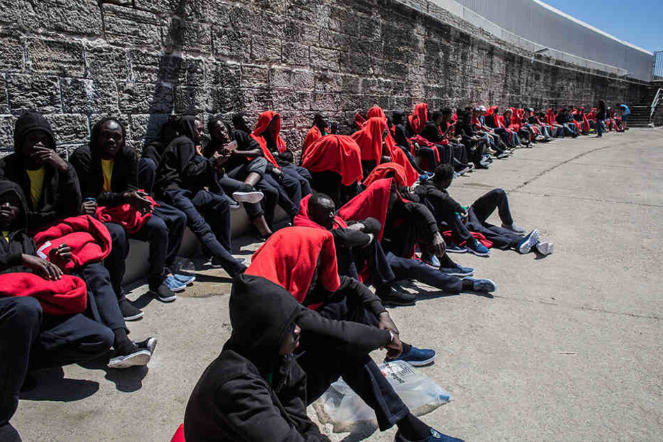 Migranten aus Afrika sitzen nach ihrer Rettung in der Straße von Gibraltar im Hafen von Tarifa in Decken gehüllt an einer Mauer.