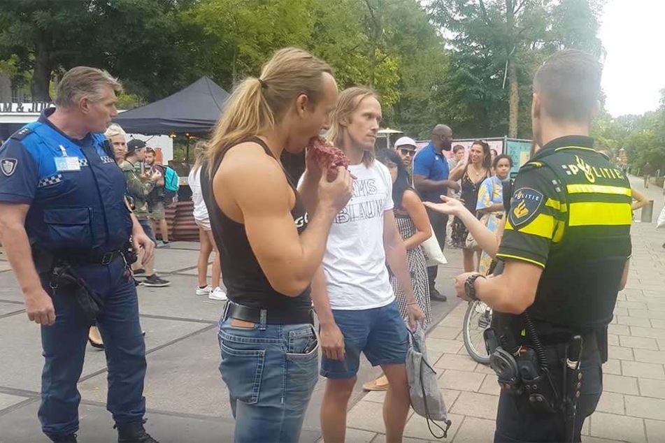 Der Mann beißt vor den Augen der entsetzten Veganer in einen rohen Batzen Fleisch.