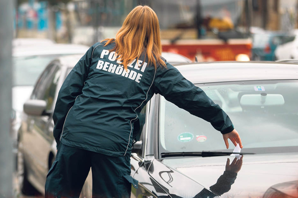 Eine Politesse klemmt ein Knöllchen unter den Scheibenwischer. In Leipzig, Dresden und Zwickau wird jetzt auch nachts gegen Falschparker hart durchgegriffen.
