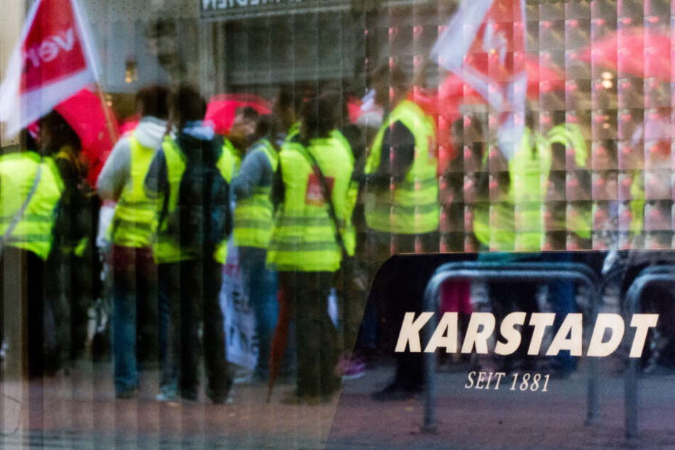 Streikende Mitarbeiter spiegeln sich im Schaufenster einer Karstadt Filiale. (Archivbild)
