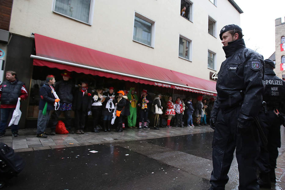 Polizisten und Narren stehen am Rosenmontag 2016 in Köln im Regen.