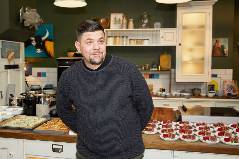 Koch Tim Mälzer steht in einer Studio-Küche vor Blechen mit Kuchen und Dessers.