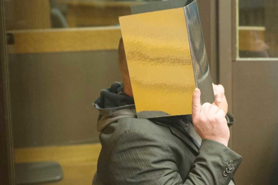 Der Angeklagte versteckt sein Gesicht hinter einem Ordner.