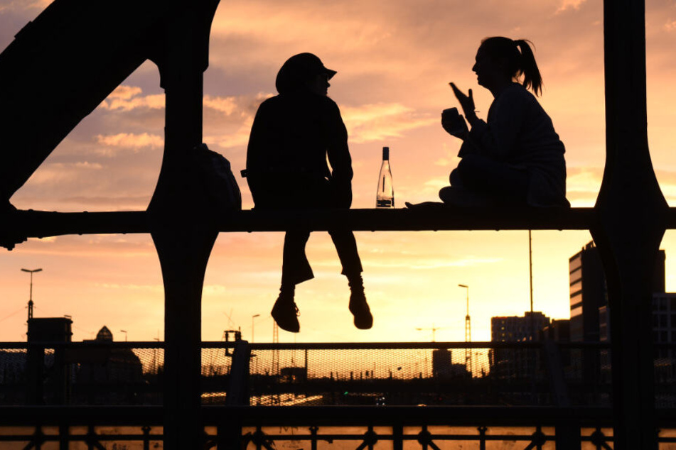 Zwei junge Frauen sitzen auf einem Stahlträger der Hackerbrücke und trinken während die Sonne unter geht. (Symbolbild)