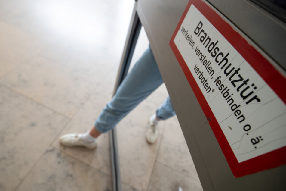 Eine Studentin steigt in einem Gebäude am FAU-Campus an der Regensburger Straße mit ihrem Fuß durch ein Loch einer defekten Brandschutztür.