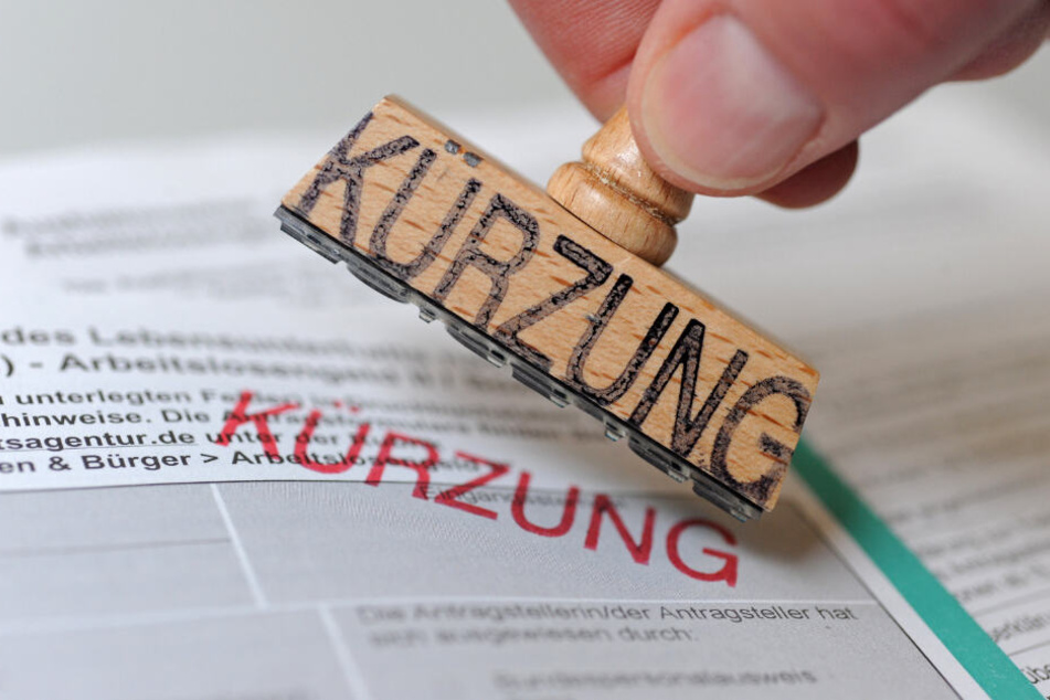 Ein Mann hält einen Stempel, auf dem das Wort "Kürzung" steht, über ein Formular zur Beantragung von Arbeitslosengeld II (Hartz-IV).
