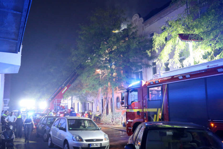 Feuerwehrleute löschen von einem Löschkorb aus den Dachstuhl des brennenden Hauses in Krefeld.