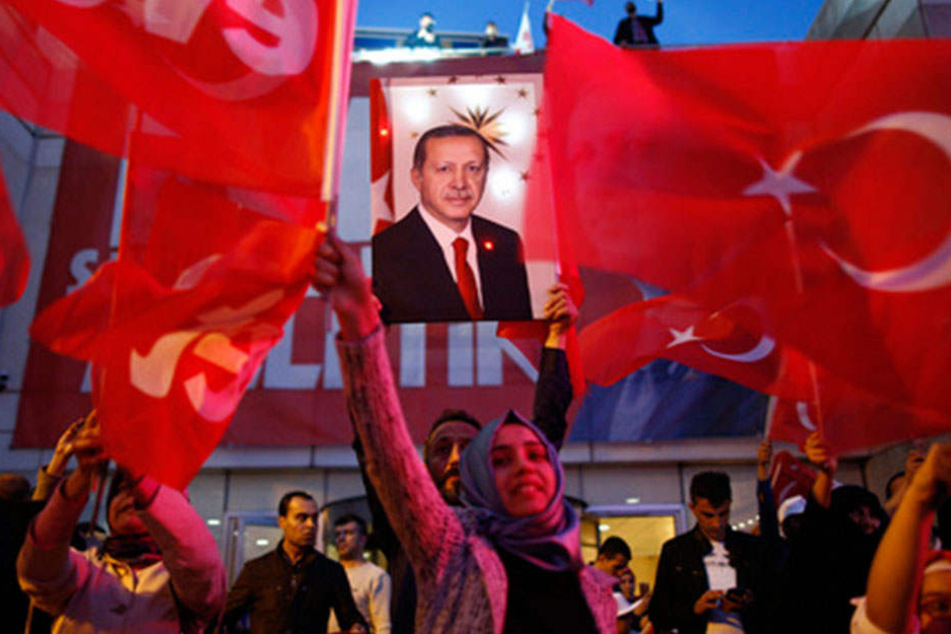 Unterstützer der türkischen Regierungspartei APK wedeln mit Fahnen und halten ein Plakat Erdogans hoch.