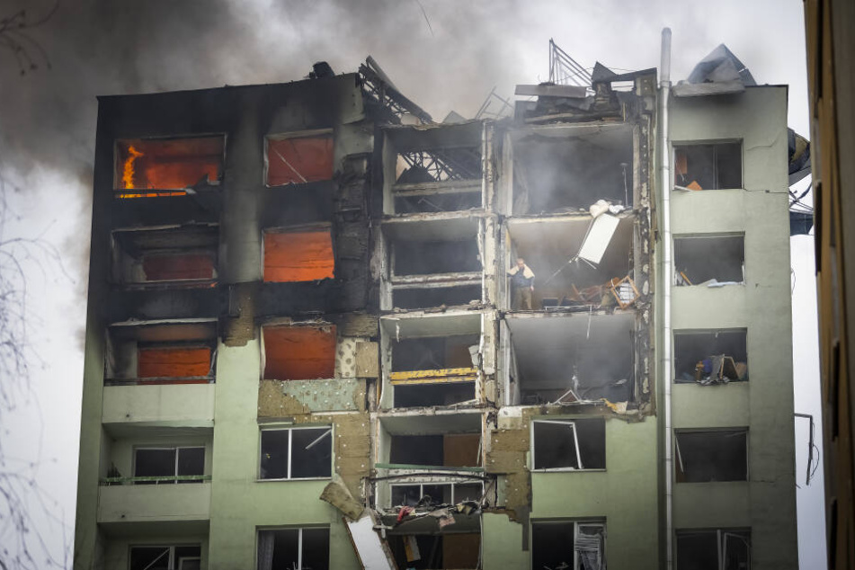Ein Bewohner steht in einem oberen Stockwerk eines zwölfstöckigen Mehrfamilienhauses, das durch eine Gasexplosion schwer beschädigt wurde, und guckt nach unten.