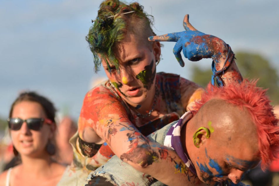 Buntbemalte Festivalbesucher gehen beim Musikfestival "Haltestelle Woodstock" in der polnischen Stadt Kostrzyn (Küstrin) über das Gelände.