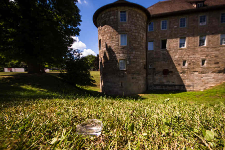 Der Boden einer zerbrochenen Glasflasche liegt im Park vor dem Burgschloss auf einer Wiese.