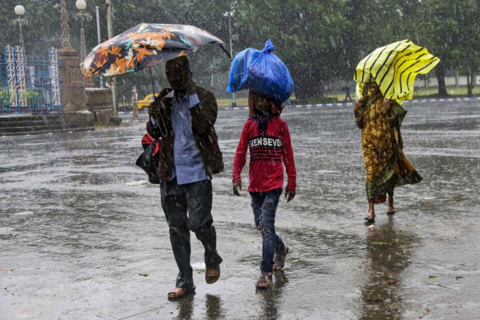 Indien, Kalkutta: Menschen gehen im Regen über die Straße und schützen sich mit Regenschirmen oder anderen Objekten vor dem Wasser.