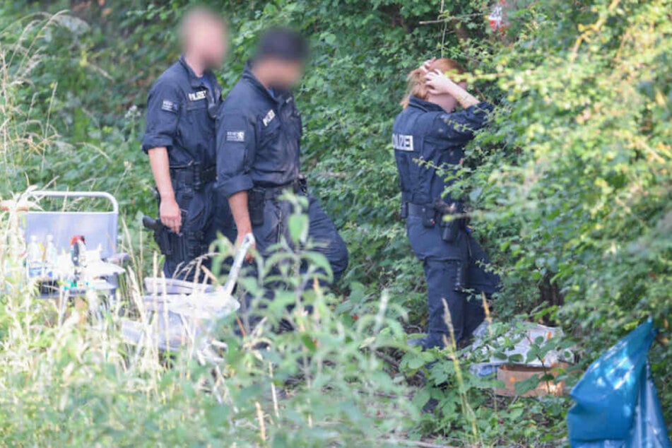Polizisten suchen den Fundort der Leiche im Gebüsch ab. (Symbolbild)