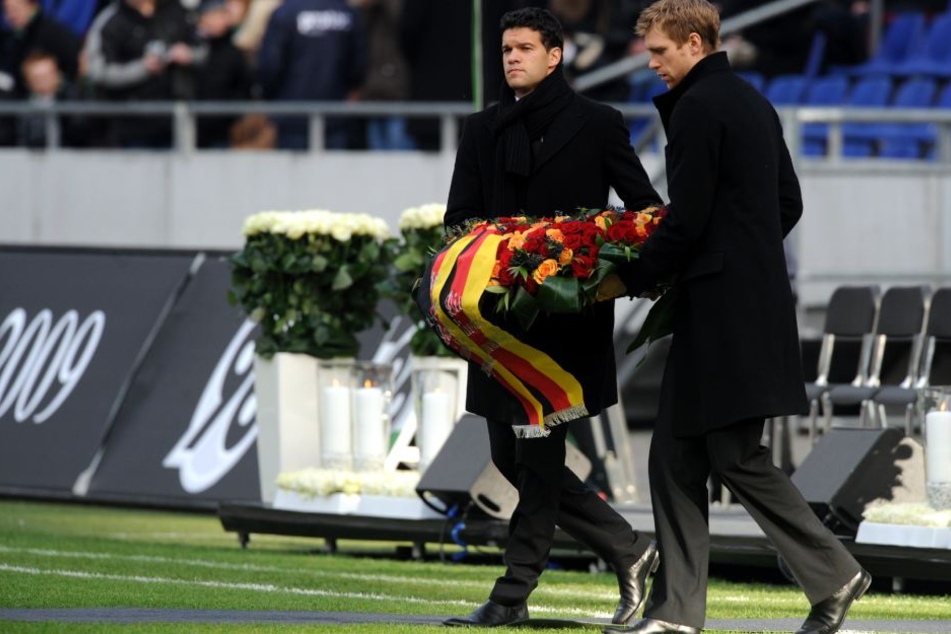 Per Mertesacker (re.) und der ehemalige Nationalmannschaftskapitän Michael Ballack (li.) tragen bei der Trauerfeier im Stadion einen Kranz zum Mittelkreis.