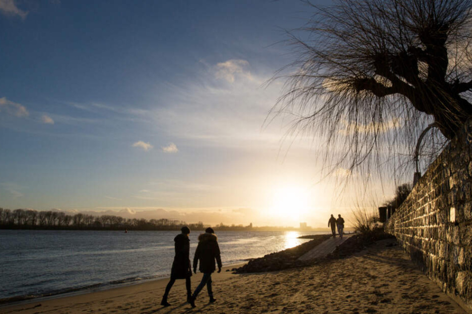 Menschen gehen am Elbstrand bei Ovelgönne im Licht des Sonnenuntergangs spazieren. So traumhaft soll es die kommenden Tage werden.