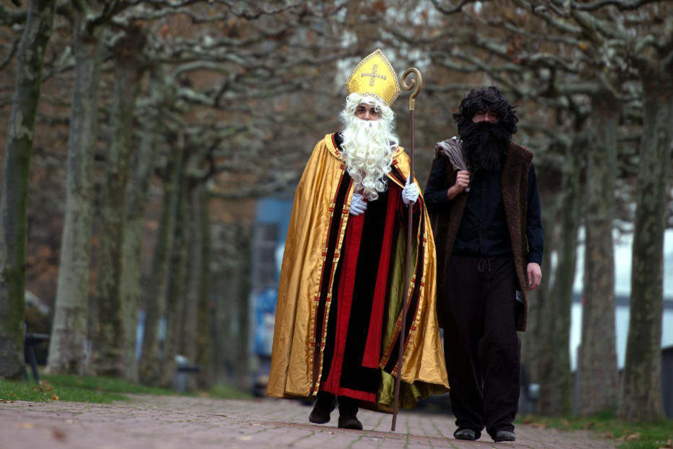 Mitglieder vom Bund der Deutschen Katholischen Jugend gehen als Nikolaus (l) und Knecht Ruprecht verkleidet am Düsseldorfer Rheinufer entlang
