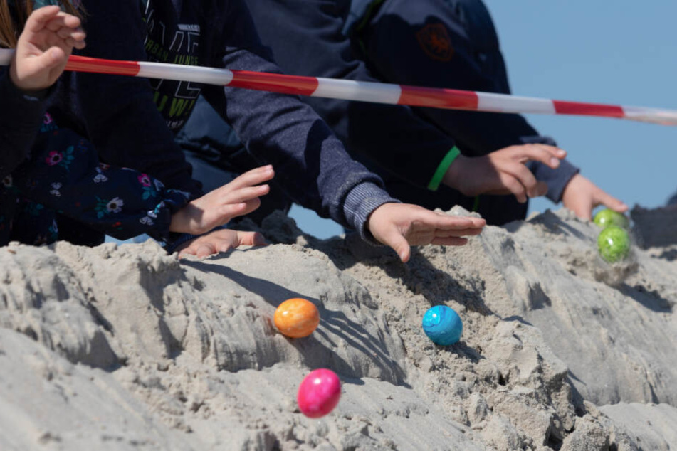 Kinder lassen Eier von einer Düne am Strand von Norderney heruntertrullern.