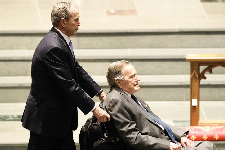 George H.W. Bush (re.) wird von seinem Sohn George W. Bush im Rollstuhl geschoben.