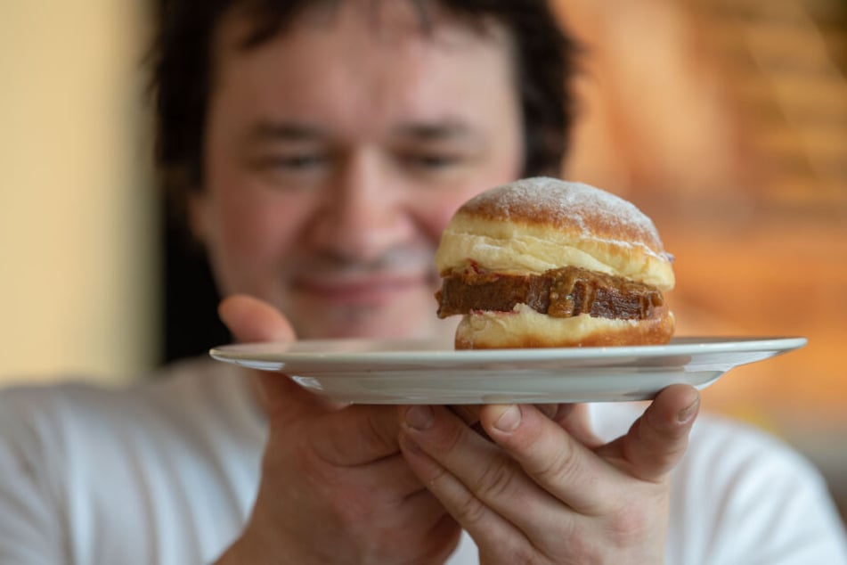 Bäckermeister Florian Perkmann hält einen Krapfen, der mit Leberkäse und süßem Senf belegt wurde in der Hand.