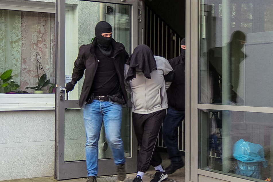 Der Tatverdächtige wird von zwei vermummten Beamten aus dem Haus geführt.