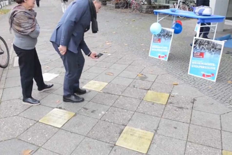 Die Wehrmachtsstolpersteine sind im Boden eingelassen, im Hintergrund steht der falsche AfD-Stand.