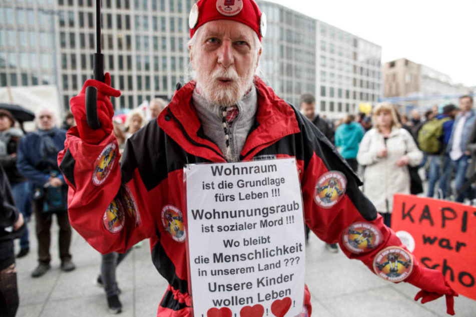 Einer der Teilnehmer trägt ein Schild, auf dem u.a. steht "Wohnraum ist die Grundlage fürs Leben!!! Wohnungsraub ist sozialer Mord!!!".