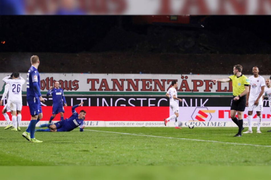 Sören Gonther (Nummer 26) schlägt die Hände vors Gesicht, während Schiedsrichter Sven Waschitzki nach dem vermeintlichen Foul auf den Elfmeterpunkt zeigt.
