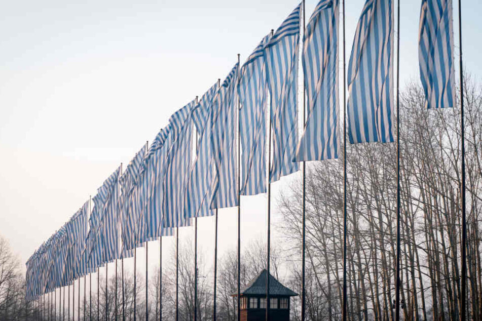 Über den Wachtürmen des früheren Konzentrationslagers Auschwitz-Birkenau wehen Fahnen im Stil der blau-weiß gestreiften KZ-Häftlingskleidung im Wind.