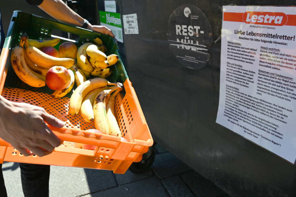 Eine Kiste voll mit Obst landet in einer Mülltonne.