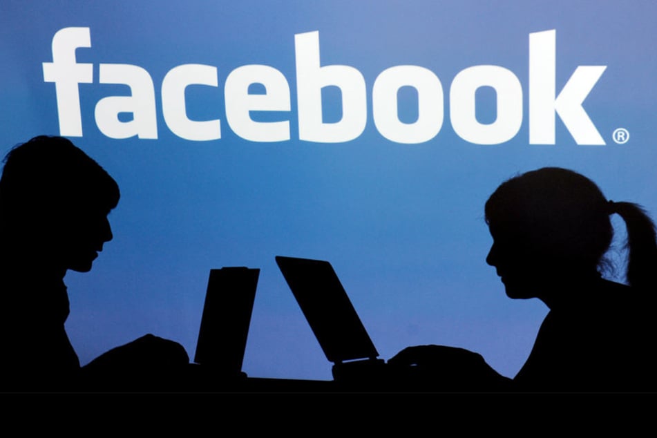 Die Schatten von Jugendlichen mit einem Laptop vor dem Schriftzug des sozialen Internet-Netzwerks Facebook.