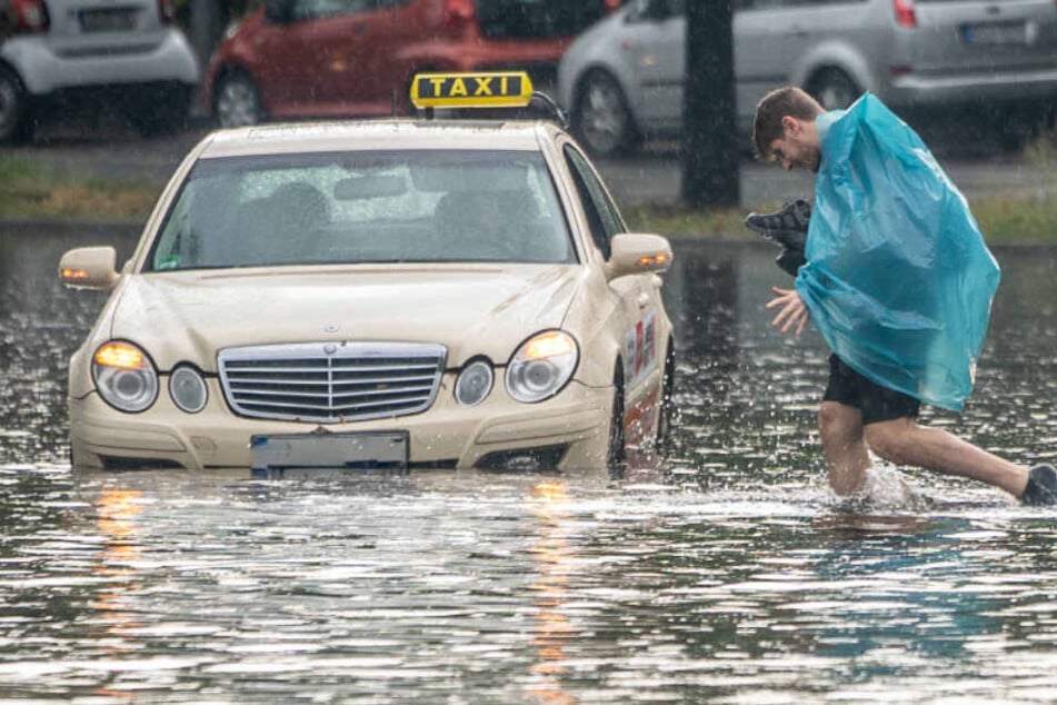 Ein Fußgänger und ein Taxi kämpfen sich durch die Regenmassen.