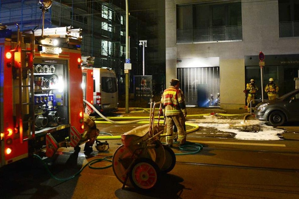 Feuerwehrmänner stehen in Berlin vor der Einfahrt einer Tiefgarage, in der mehrere Autos in Brand geraten waren.