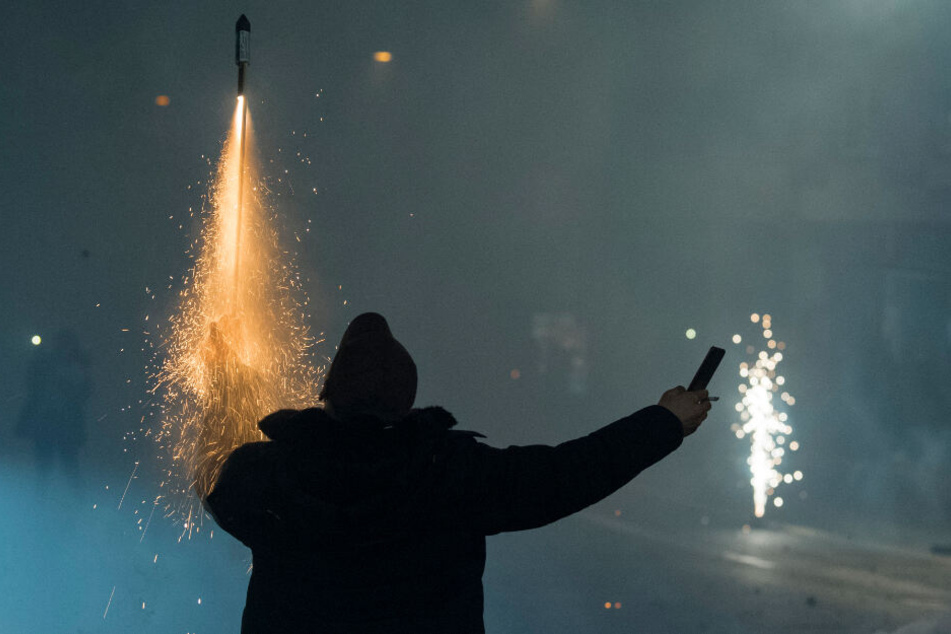 Während er mit der linken Hand eine brennende Rakete hält, filmt sich ein Mann bei der Aktion selbst mit seinem Smartphone.