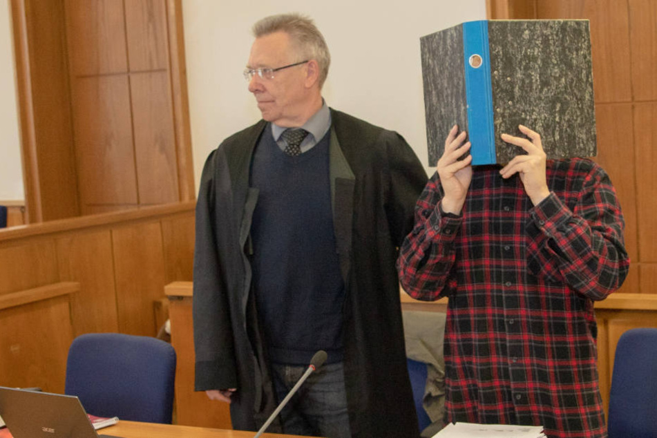 Der Angeklagte versteckt sein Gesicht hinter einem Aktenordner.