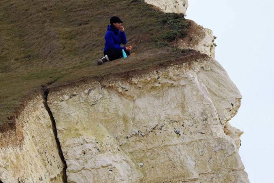 Die Frau sitzen auf der Abbruchkante, unter ihr zieht sich ein riesiger Riss durch den Kreidefelsen.