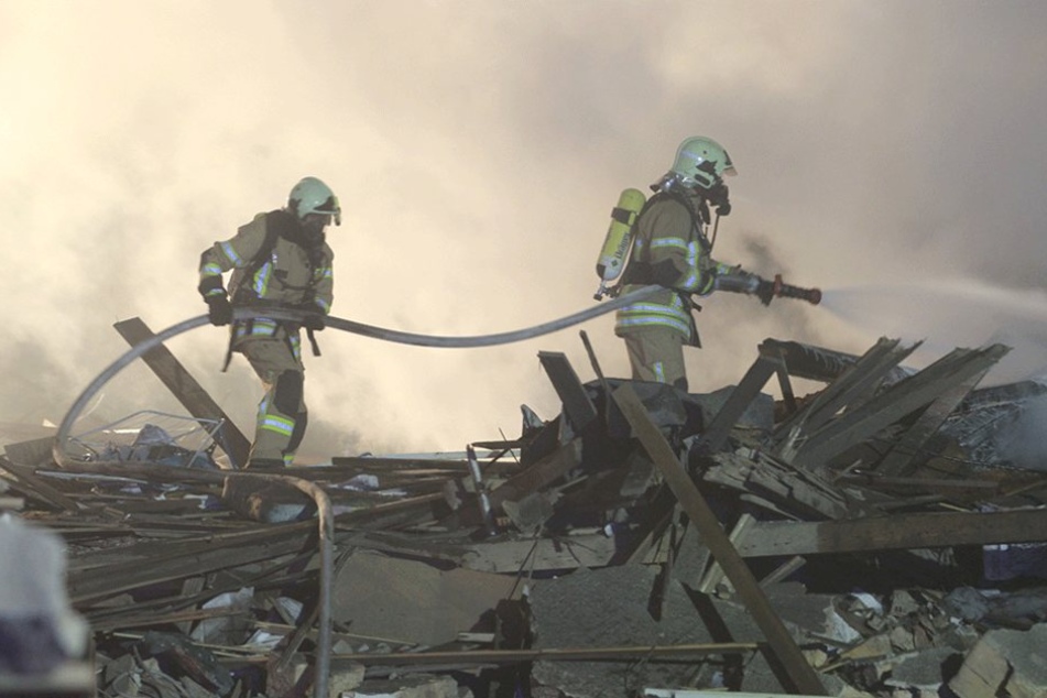 Feuerwehrmänner löschen Flammennester in den Trümmern.