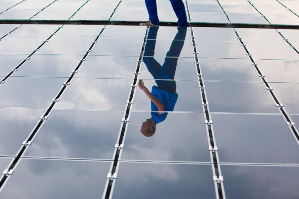 Ein Elektriker läuft für Wartungsarbeiten über ein Dach mit Solarplatten (Symbolbild).