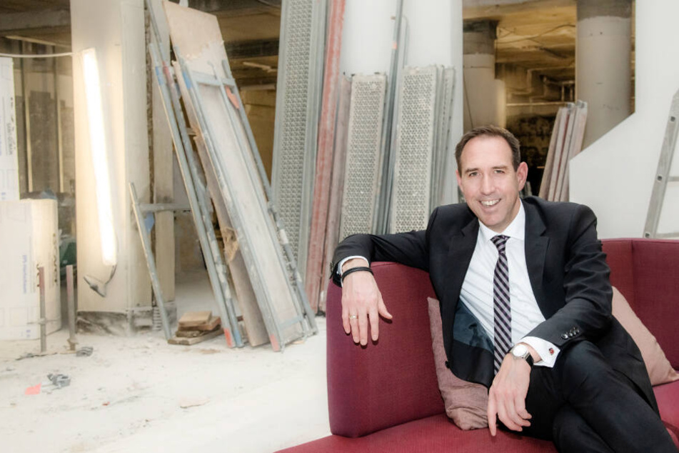 Hotel-Direktor Hannes Dreher sitzt auf einem roten Sofa auf der Baustelle.