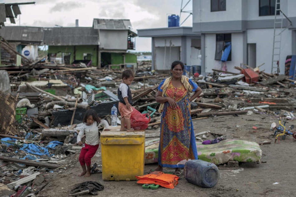 Eine Frau und ihre Kinder stehen zwischen den Trümmern in einem vom Tsunami verwüsteten Dorf.