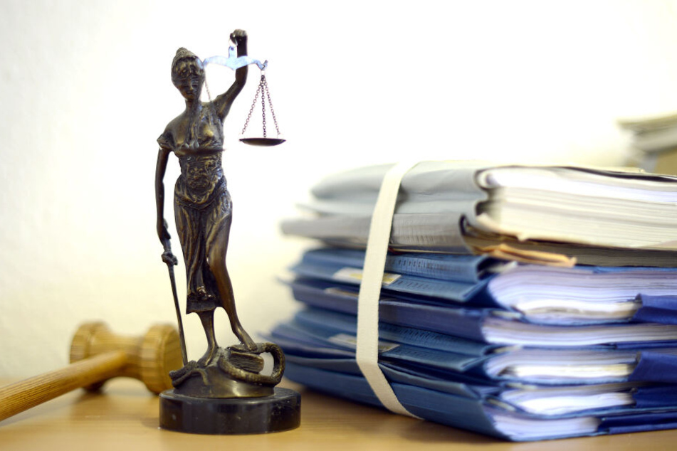Ein Modell der Justitia steht in einem Raum eines Richters neben einem Holzhammer und einem Aktenstapel (Symbolbild).