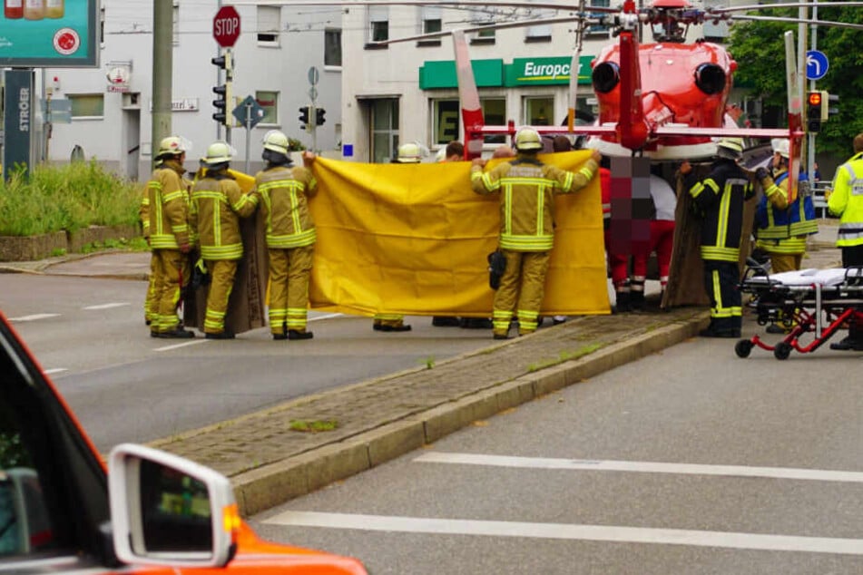 Feuerwehrleute halten eine Decke hoch, um die Sicht auf Verletzte zu verdecken.