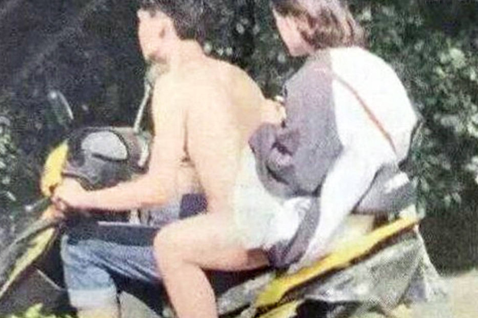 Die beiden sitzen auf dem Motorroller, der Fahrer scheinbar nackt.
